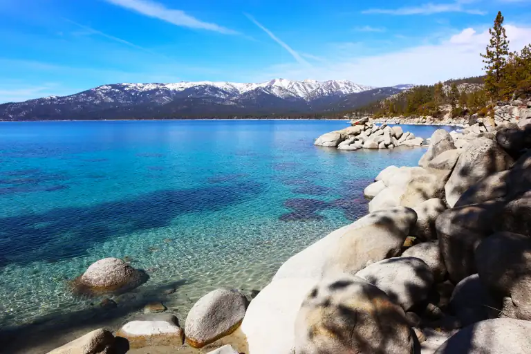 a rocky Lake Tahoe shore with clear blue water and mountains in the background